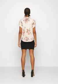 Blusa floral de mangas curtas com fundo bege e padrões coloridos de flores, combinada com uma saia mini preta e justinha.