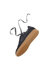 Black sneaker with a textured upper, black laces, and a gum rubber sole featuring a herringbone pattern. Accented logo on the side.