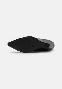 Semelle de chaussure en caoutchouc noir avec une forme pointue, présentant un fond texturé pour l'adhérence et des détails de marque sur le côté.