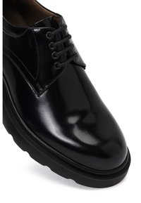 Chaussure en cuir noir avec une finition brillante, présentant un bout rond, un laçage à six œillets et une semelle épaisse et texturée.