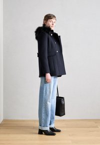 Jūrinės vilnos mišinio paltas su dirbtiniu kailio apykakle, dvigubo eilės mygtukais, auksiniais mygtukais, derinamas su šviesios džinsinės kelnės ir juoda rankine.