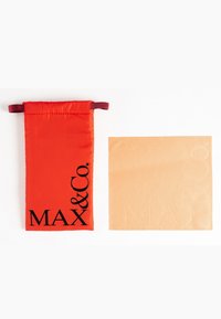 Röd tygpåse med dragsko, med svart "MAX & Co."-logotyp. Intill en ljusbrun kvadrat med präglade bokstäver.