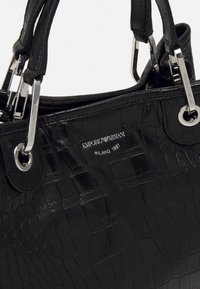 Svart handväska i krokodilstruktur med silverdetaljer och Emporio Armani Milano 1981-logotyp präglad på framsidan.