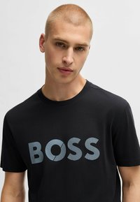 T-shirt noir à manches courtes en coton, avec un grand graphique "BOSS" en bleu clair avec une texture rayée sur la poitrine.