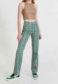 Pantalons évasés avec un motif circulaire bleu et beige ; associés à un haut sans manches marron et des baskets à accents verts. Texture de tissu lisse.