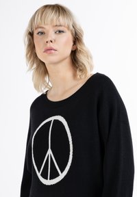 Maglione nero con un grande simbolo della pace bianco. Tessuto morbido, scollatura rotonda e vestibilità ampia, progettato per il comfort e l'uso quotidiano.