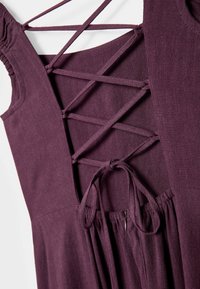 Dos de robe violet profond avec des liens en tissu croisés et un nœud au-dessus d'une ceinture froncée et une fermeture éclair cachée.