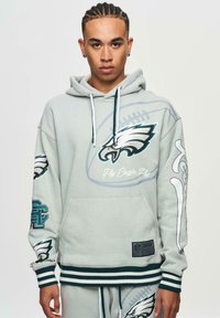 Ljusgrå sweatshirt med Eagles-logga, framficka, ribbad mudd och nederkant, samt grafiska detaljer på ärmarna. Tillverkad av mjukt, strukturerat material.