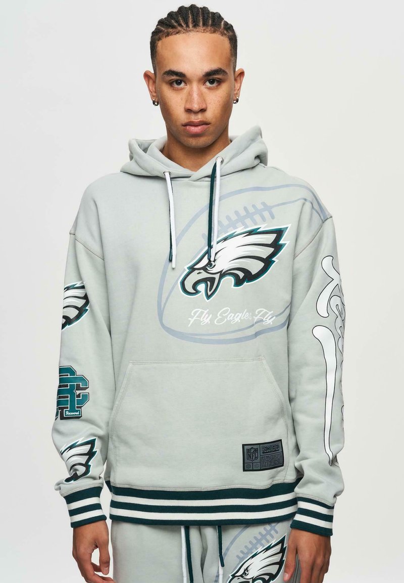 Ljusgrå sweatshirt med Eagles-logga, framficka, ribbad mudd och nederkant, samt grafiska detaljer på ärmarna. Tillverkad av mjukt, strukturerat material.