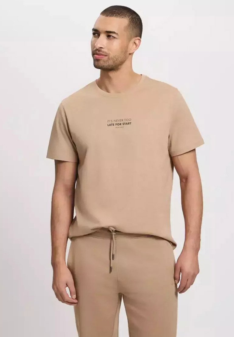 Beżowa bawełniana koszulka z krótkim rękawem z czarnym nadrukiem tekstu na klatce piersiowej, w zestawie z pasującymi beżowymi spodniami.