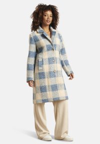 Wollmischung karierten Mantel in Hellblau und Creme, mit Reverskragen, vorderen Knöpfen und Seitentaschen. Trägt man über beigen weit geschnittenen Hosen.