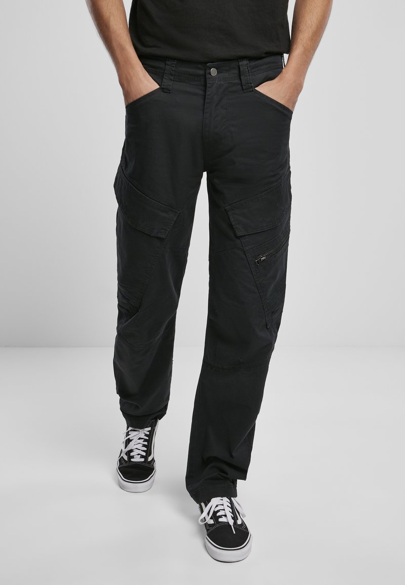 Schwarze Cargo-Hosen aus Baumwollmaterial. Verfügt über mehrere Taschen, eine lockere Passform und Reißverschluss-Akzente. Kombiniert mit schwarz-weißen Sneakers.