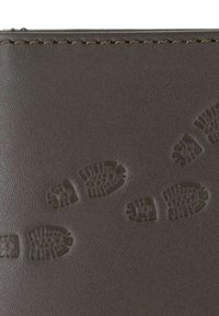 Gros plan sur un cuir foncé avec motif de semelle de botte embossé et couture visible le long du bord supérieur.