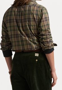 Rutig skjorta i grönt och burgundy, tillverkad av bomull, med uppvikta ärmar och rundad nederkant; matchad med mörkgröna kordbyxor.