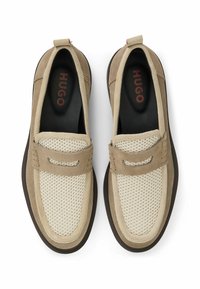 Tan- und beigefarbene Slipper mit Obermaterial aus Wildleder und Mesh, Gummisohle und einer dekorativen Akzentuierung auf dem Obermaterial. Markenname "HUGO" ist innen sichtbar.