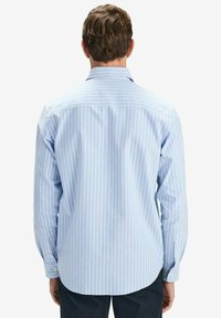 Vaaleansininen raidallinen nappipaita, jossa on suora takaosa ja pitkät hihat, ja joka sisältää valkoisia pystyraitoja sekä hihnapainikkeet.