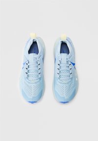 Hellblaue Sportschuhe mit einem strukturierten Mesh-Obermaterial, Belüftungsöffnungen für Atmungsaktivität und einem blauen Akzent an der Seite. Mit gelbem Zugband.