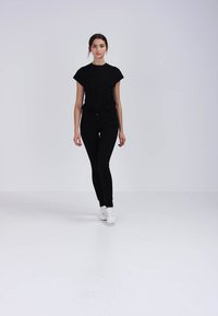 Camiseta negra de manga corta combinada con jeans skintight negros y zapatillas blancas, sobre un fondo claro y liso.