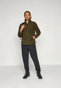 Olivová fleecová bunda so zipsom, čierne nohavice a pevné čierne turistické topánky, s hladkou textúrou a funkčným dizajnom.