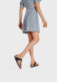 Zwarte platform sandalen met een kurken wedge hak, met een brede band en een verstelbare gesp, gedragen met een lichte spijkerjurk.