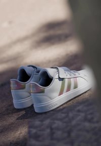Vita sneakers med tre horisontella ränder i rosa och grönt. Har en slät yta, rundad tå och en vadderad krage för komfort.