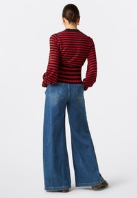 Rot und schwarz gestreiftes Langarmshirt mit tapered Manschetten, kombiniert mit weit geschnittenen blauen Jeans aus Denim mit Gesäßtaschen und rohen Abschlüssen.