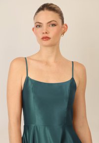 Teal satiinimekko, jossa on neliömäinen pääntie ja ohuet olkaimet, istuva yläosa ja levenevä hameosa, sileä pinta ja minimalistinen muotoilu.