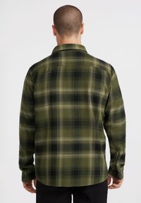 Groene geruite flanellen overhemd, met zwarte en crèmekleurige ruitpatronen, een kraag en knoopmanchetten. Zachte stof met een losse pasvorm.