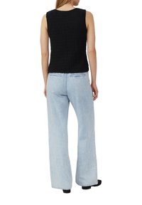 Schwarzes, strukturiertes, ärmelloses Oberteil, kombiniert mit hellblauen, weit geschnittenen Jeans. Hat ein einfaches Design mit gerader Silhouette und minimalen Details.