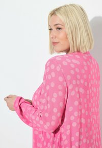 Pinker Kimono mit Punkten, aus leichtem, strukturiertem Stoff; verfügt über lange Ärmel und eine lockere Passform, die eine entspannte Silhouette betont.