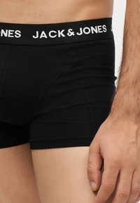 Άνδρας που φοράει μαύρα μποξεράκια Jack & Jones με ορατό λογότυπο στη μέση και χέρι που ακουμπά δίπλα στον μηρό.