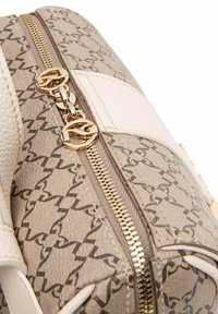 Borsa beige con un motivo testurizzato, dettagli in pelle bianca, hardware dorato e una chiusura lampo dorata ben visibile.