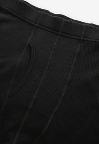 Sous-vêtements thermiques noirs avec un tissu texturé, une taille élastique et des ouvertures fonctionnelles, dotés de coutures plates pour plus de confort.