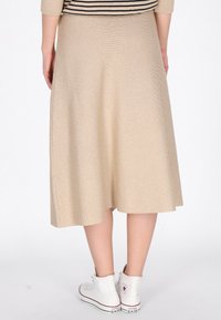 Jupe beige, mi-longue, en forme de A, en tissu texturé, avec un motif subtil, associée à des baskets montantes blanches.