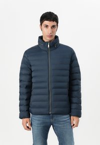 Navy blue puffer jacket featuring a high collar, quilted design, front zip closure, and side pockets; made from lightweight, water-resistant material.