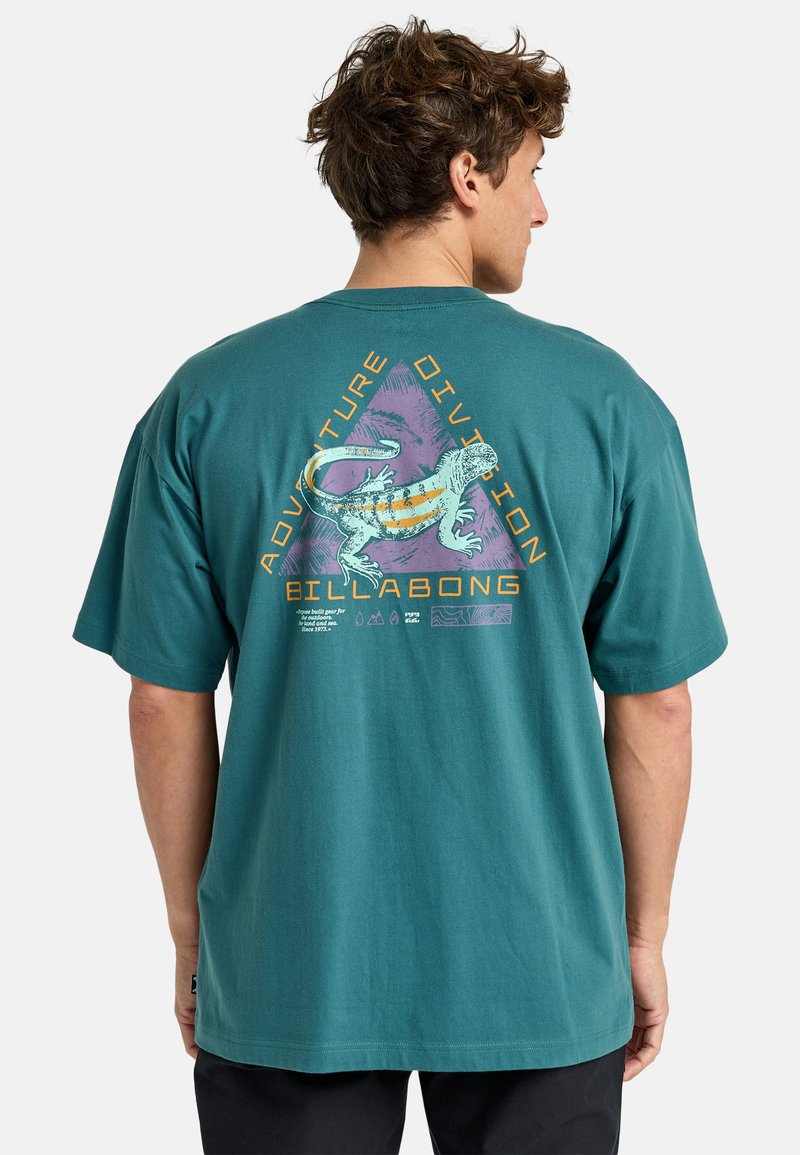 Teal cotton t-shirt featuring a colorful lizard graphic with the text "ADVENTURE DIVISION" on the back. Short sleeves, relaxed fit.