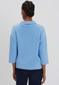 Maglietta azzurra chiaro a maniche lunghe con colletto e vestibilità ampia. Tessuto morbido e cuciture delle spalle scese. Design semplice senza motivi o accenti.