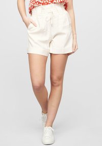 Lys beige elastiske shorts med stikklommer og rullet erme, laget av et glatt stoff. Kombinert med hvite sneakers.