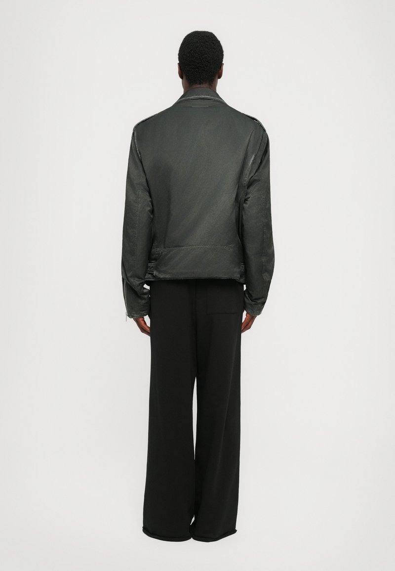 Black woven jacket with a smooth texture, featuring a classic collar and loose fit, paired with wide-leg black trousers.