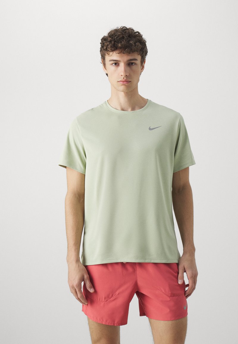 Lys grøn kortærmet træningsskjorte med rund hals og et gråt Nike-logo på brystet, parret med lyserøde shorts.