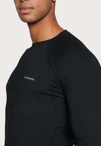 Camiseta deportiva de manga larga negra, confeccionada con un tejido suave. Presenta un cuello redondo y un logo sutil en el pecho.