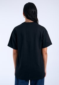 Camiseta de algodón negra de corte oversized con escote redondo, mangas cortas y dobladillo recto, que presenta un diseño mínimo en la parte trasera.