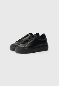 Tenis pretos com um cabedal de couro liso, design de atacadores, colarinho macio e sola de borracha em plataforma. Branding minimalista de um lado.