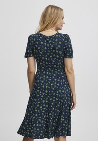 Námořnické šaty s krátkými rukávy, zdobené květinovým vzorem v zelené barvě. Jsou vyrobeny z měkké látky, mají rozšířený střih a kulatý výstřih.