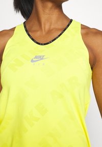 Top sin mangas de Nike en tela amarilla brillante con un ribete negro. Presenta un patrón de malla y el logo "NIKE AIR" en gris en el centro.