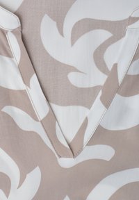 Tissu beige et blanc à motif de feuilles avec un col en V et des détails de couture visibles.