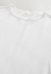 White, ribbed fabric t-shirt featuring a rounded neckline. Label includes "NEXT THERMOGEN" and care details. Smooth texture, minimalist design.