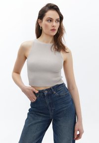 Béžový žebrovaný crop top spárovaný s tmavě modrými džíny se zvýšeným pasem. Top má bezramínkový design a kulatý výstřih.