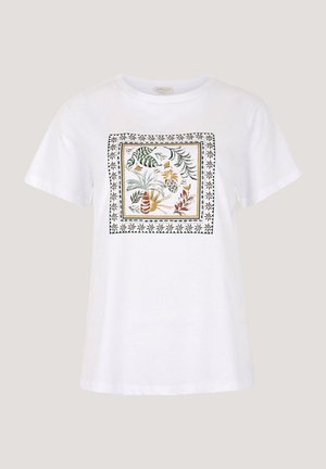 T-shirt en coton blanc présentant un imprimé floral carré avec des accents verts, jaunes et bruns, bordé d'un motif décoratif noir.