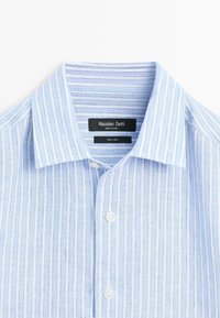 Chemise en lin à rayures verticales bleu clair et blanches, à col, avec boutons blancs et étiquette de marque Massimo Dutti à l'intérieur du col.
